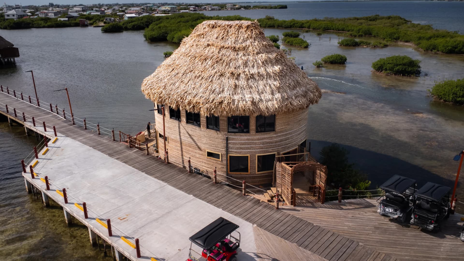 The Mayan, a round building with a tall palm-thatch roof, beside a wooden boardwalk over the lagoon at Lina Point.