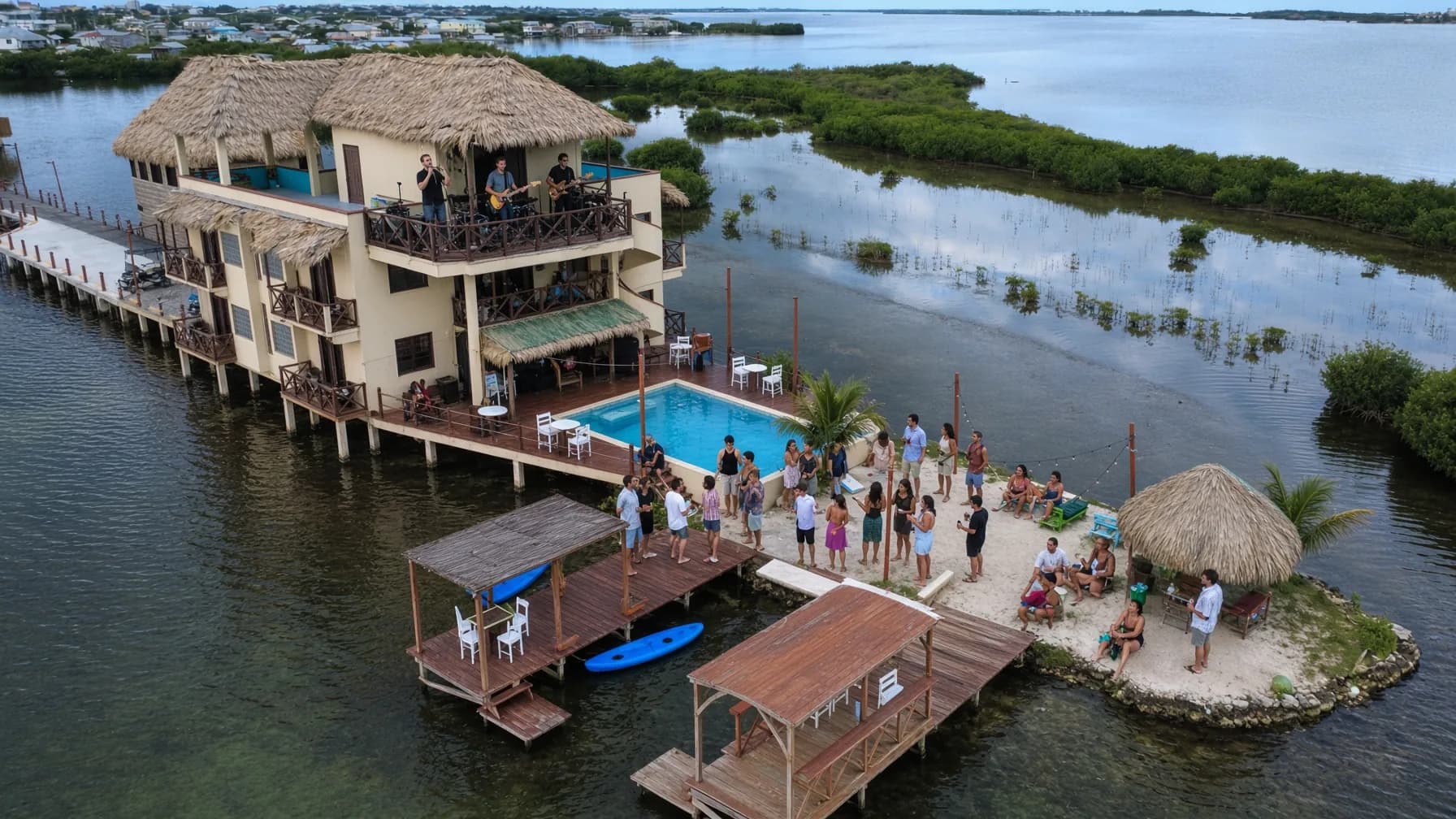 A band playing on Lina Point's balcony while guests gather by the pool and sandbar.